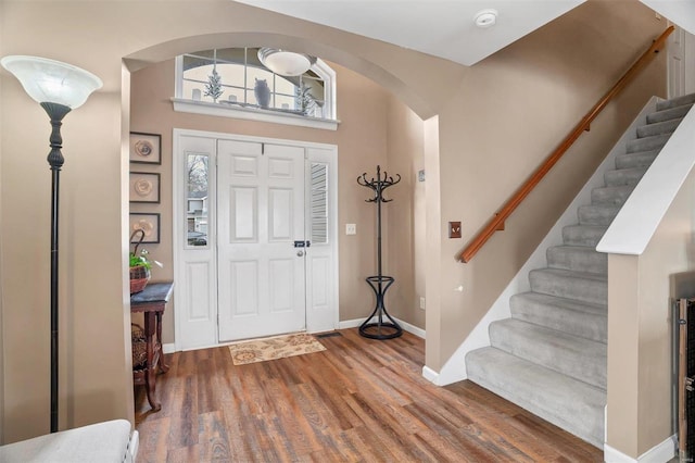 entrance foyer with stairs, arched walkways, baseboards, and wood finished floors