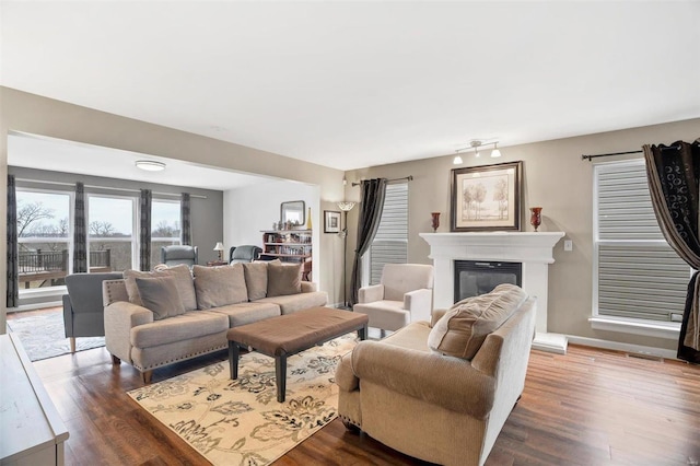 living room featuring dark wood-type flooring, a glass covered fireplace, and baseboards