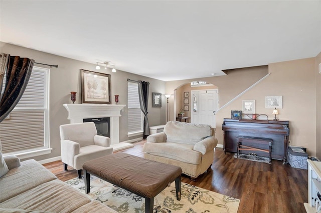 living room featuring arched walkways, wood finished floors, a glass covered fireplace, and baseboards