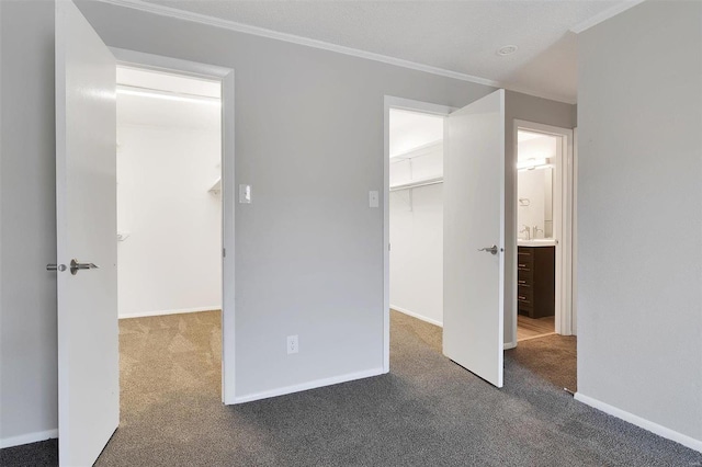 unfurnished bedroom with a walk in closet, a closet, carpet, crown molding, and baseboards