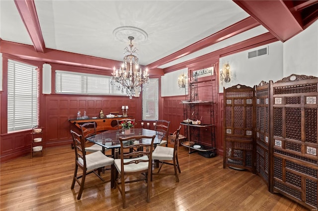 dining room with beam ceiling, a wainscoted wall, visible vents, wood finished floors, and a chandelier