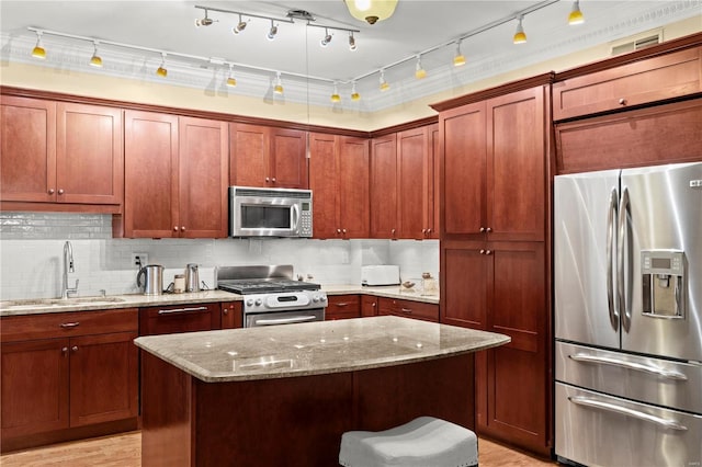 kitchen with backsplash, appliances with stainless steel finishes, a kitchen island, a sink, and light stone countertops