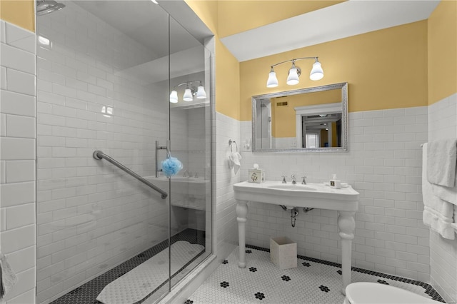 bathroom with tile patterned flooring, a wainscoted wall, a sink, tile walls, and a stall shower