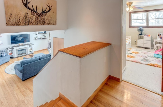 living room featuring a ceiling fan, baseboards, wood finished floors, and a glass covered fireplace