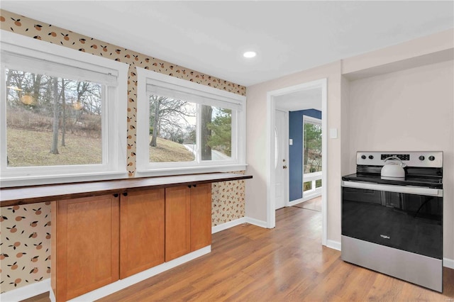 kitchen featuring electric stove, light wood finished floors, brown cabinets, and baseboards