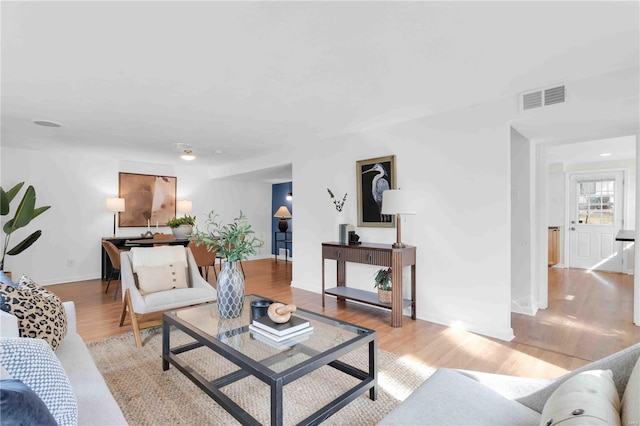 living room with light wood finished floors, visible vents, and baseboards