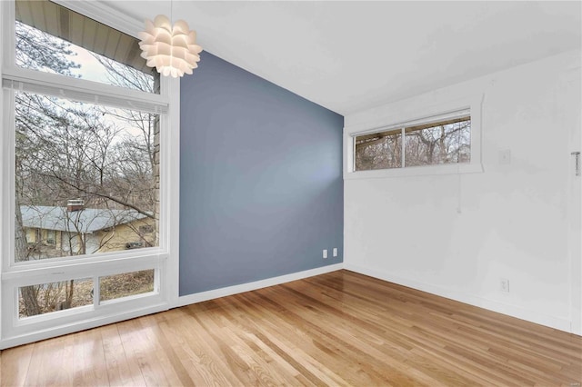 empty room featuring baseboards, a notable chandelier, wood finished floors, and a healthy amount of sunlight