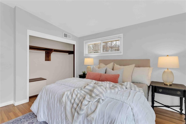 bedroom with a closet, wood finished floors, visible vents, and baseboards