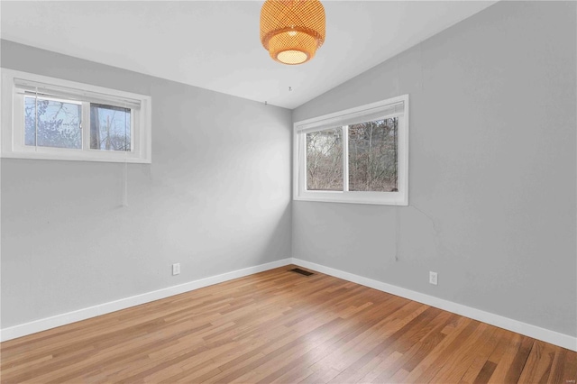 empty room featuring lofted ceiling, visible vents, light wood-style flooring, and baseboards