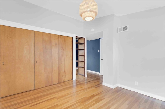 unfurnished bedroom with a closet, wood finished floors, visible vents, and baseboards