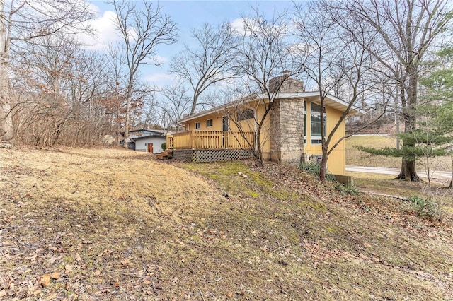 view of side of property featuring stone siding, a chimney, and a deck