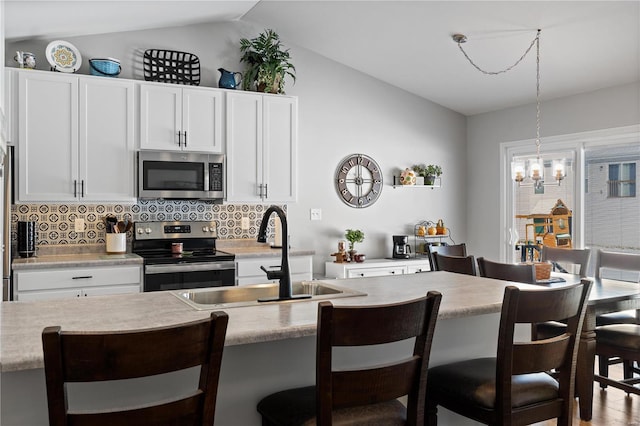 kitchen featuring white cabinets, vaulted ceiling, light countertops, appliances with stainless steel finishes, and an island with sink