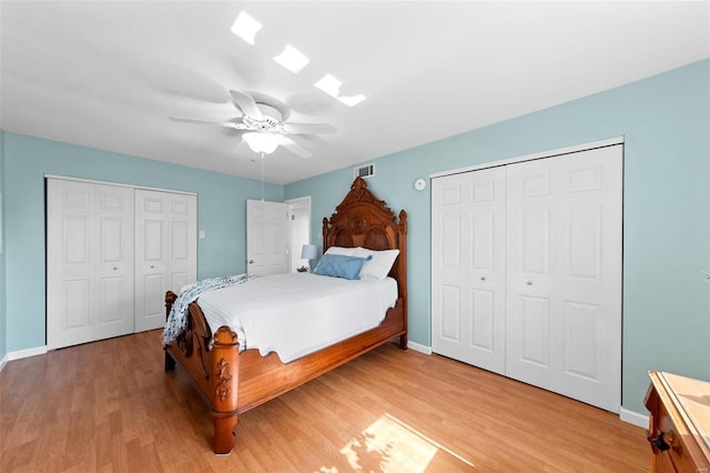 bedroom with baseboards, visible vents, a ceiling fan, light wood-style floors, and two closets