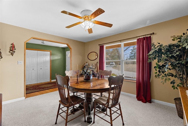 dining area featuring light carpet, baseboards, arched walkways, and ceiling fan