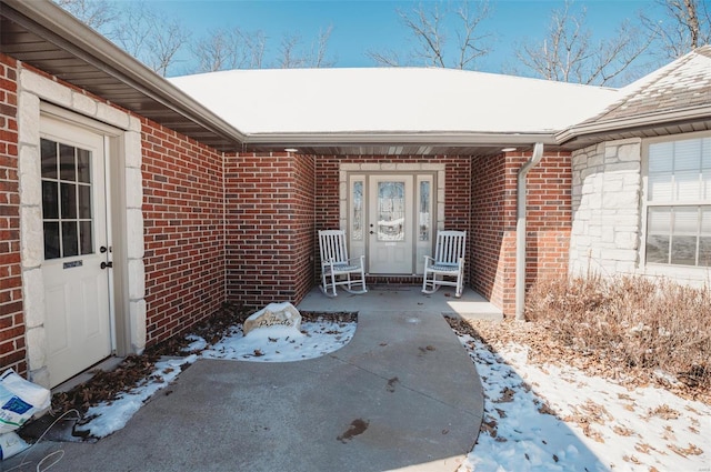 snow covered property entrance with a patio and brick siding