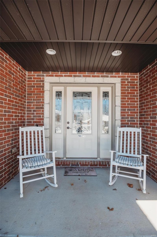 view of exterior entry featuring covered porch and brick siding