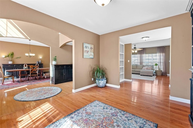 interior space featuring baseboards, arched walkways, wood finished floors, and ceiling fan with notable chandelier