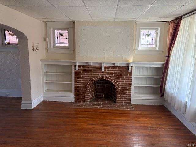 unfurnished living room with arched walkways, a fireplace, dark wood finished floors, and baseboards