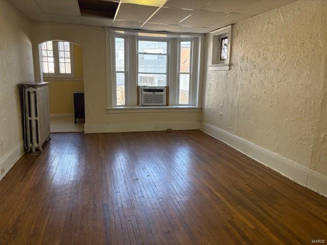 spare room featuring dark wood-style floors, a drop ceiling, baseboards, and radiator