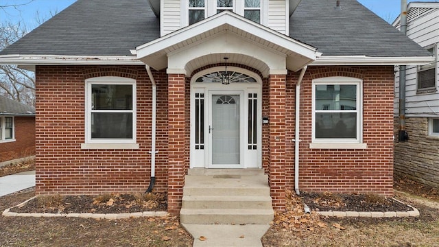 view of exterior entry featuring a shingled roof and brick siding