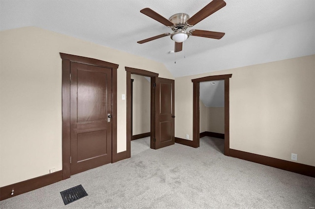 unfurnished bedroom with ceiling fan, light colored carpet, visible vents, baseboards, and vaulted ceiling