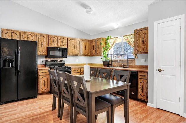 kitchen featuring lofted ceiling, black appliances, brown cabinetry, and light countertops