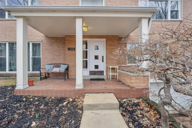 doorway to property featuring brick siding and a porch