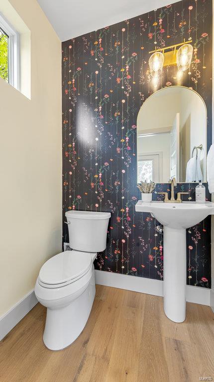 half bathroom with wood finished floors, baseboards, toilet, and wallpapered walls