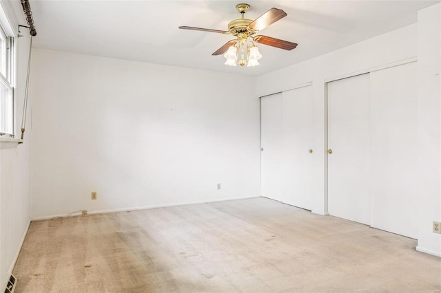 unfurnished bedroom featuring ceiling fan, carpet floors, and two closets