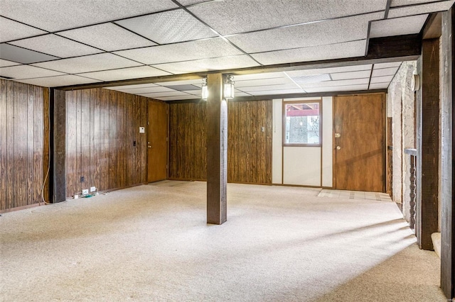 basement with carpet floors, wooden walls, and a drop ceiling