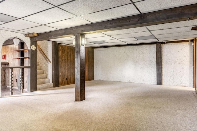 finished basement with a paneled ceiling, stairway, and carpet