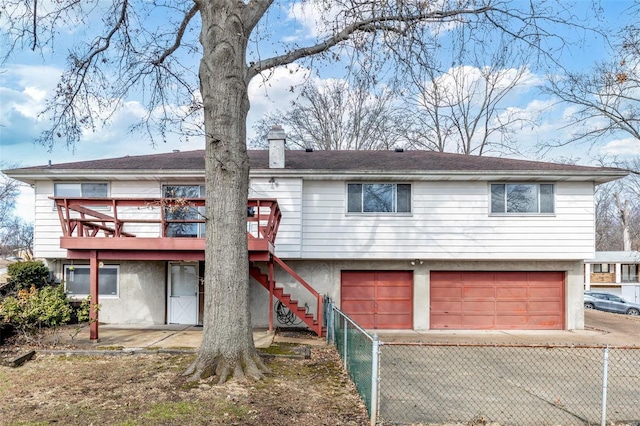 rear view of property featuring a garage, a chimney, stairway, fence, and a deck