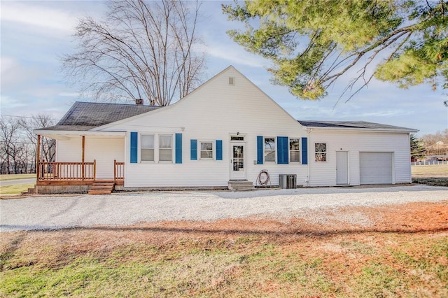 ranch-style home featuring gravel driveway, an attached garage, central AC unit, and covered porch