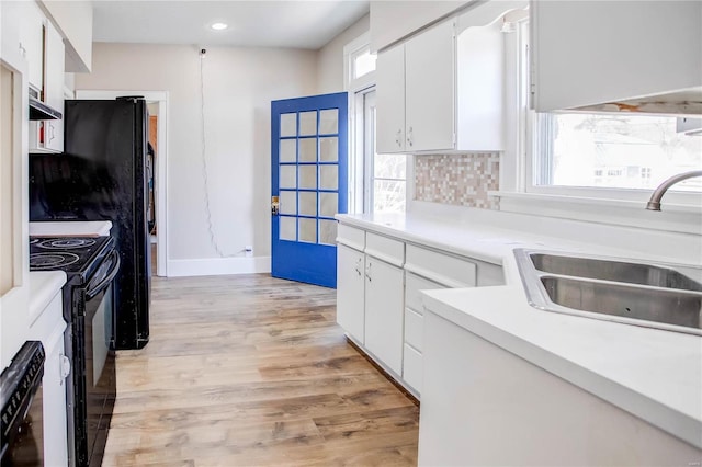 kitchen with a sink, black range with electric cooktop, wall chimney exhaust hood, white cabinets, and light wood finished floors