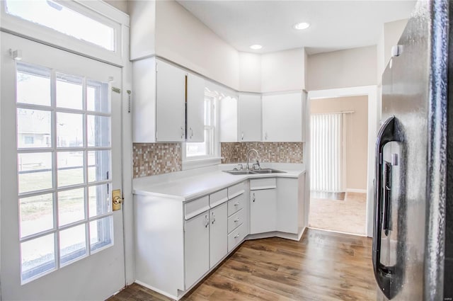 kitchen with a sink, light countertops, white cabinets, tasteful backsplash, and black fridge