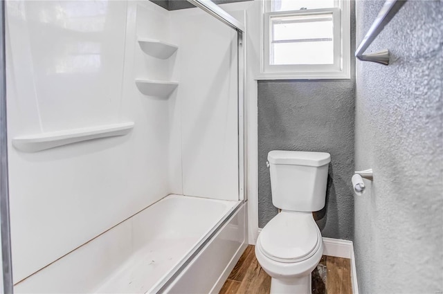 full bathroom featuring toilet, wood finished floors, baseboards, and a textured wall