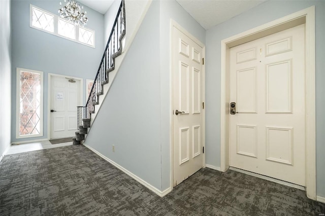 entrance foyer with stairs, dark carpet, a notable chandelier, and baseboards