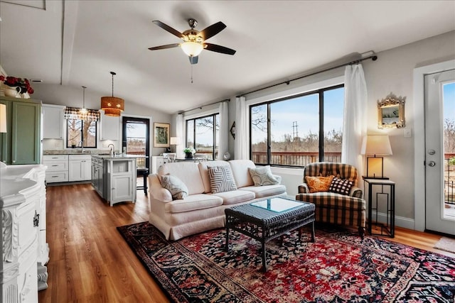 living area with lofted ceiling, ceiling fan, baseboards, and wood finished floors