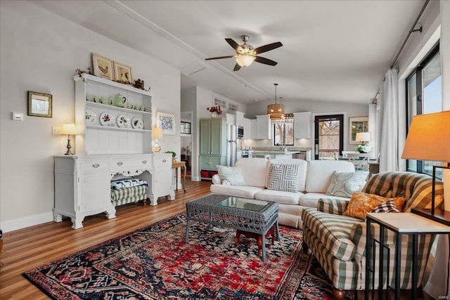 living room with a ceiling fan, lofted ceiling, baseboards, and light wood finished floors