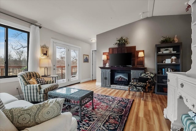 living room featuring vaulted ceiling, light wood-type flooring, a fireplace, and baseboards