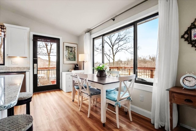 dining space with lofted ceiling, baseboards, and light wood-style floors