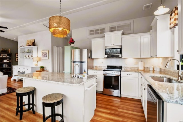 kitchen featuring stainless steel appliances, a sink, light wood-style floors, white cabinets, and decorative backsplash