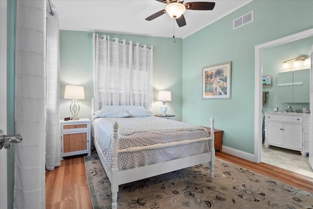 bedroom with baseboards, visible vents, a ceiling fan, wood finished floors, and ensuite bathroom