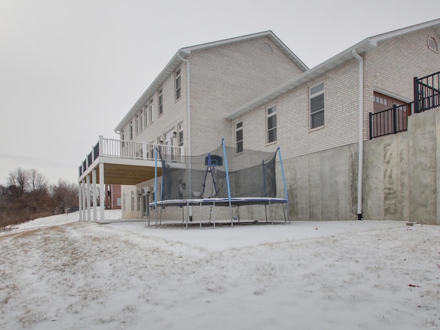 snow covered rear of property with a trampoline, brick siding, and a garage