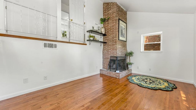 unfurnished living room with a brick fireplace, baseboards, visible vents, and wood finished floors