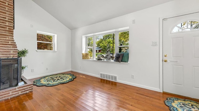 foyer entrance featuring vaulted ceiling, a brick fireplace, wood finished floors, and visible vents