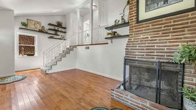 unfurnished living room with lofted ceiling, wood finished floors, baseboards, stairway, and a brick fireplace