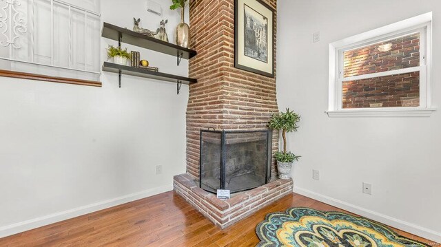 living area with a brick fireplace, baseboards, and wood finished floors