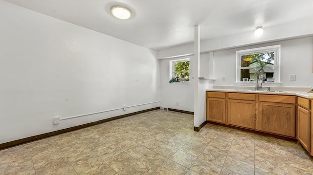 interior space featuring brown cabinetry, light countertops, a sink, and baseboards