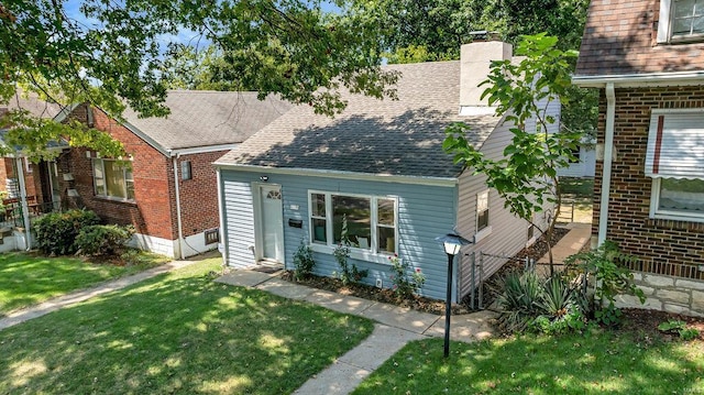 view of front facade with roof with shingles, brick siding, a chimney, and a front yard